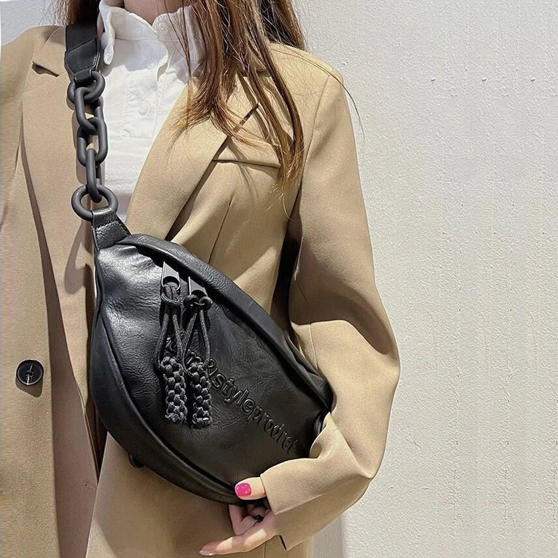 Frau mit schwarzer Leder-Umhängetasche, Kettengurt, beige Blazer, modisch, elegant.