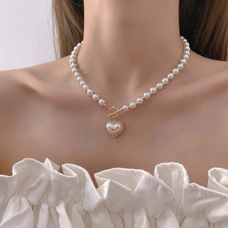 Frau mit Perlenkette und herzförmigem Anhänger, eleganter Schmuck, weißes Oberteil.