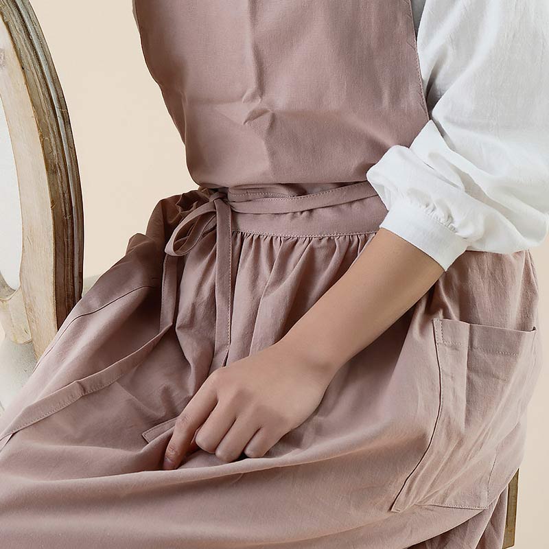 Frau in rosa Baumwollschürze, sitzt auf Stuhl, Küchenschürze mit Taschen, elegantes Design.