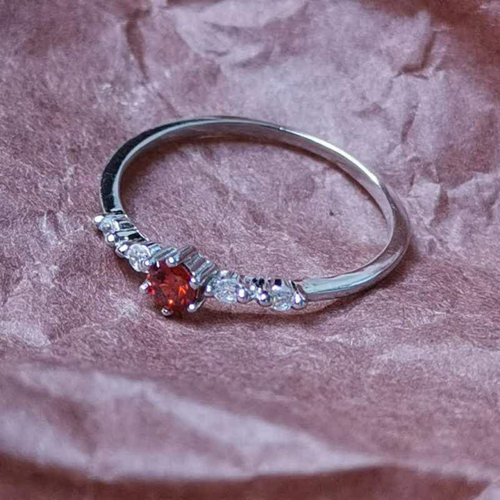 Silberring mit rotem Edelstein und Diamanten, elegantes Schmuckdesign, auf rosa Hintergrund.