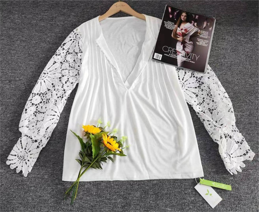 Weiße Bluse mit Spitzenärmeln, V-Ausschnitt, auf grauem Hintergrund, neben Sonnenblumen.