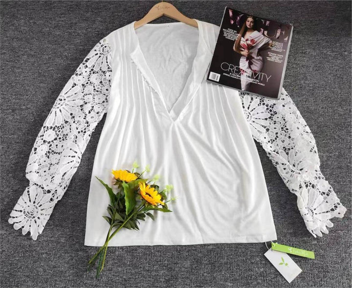 Weiße Bluse mit Spitzenärmeln, V-Ausschnitt, auf grauem Hintergrund, neben Sonnenblumen.