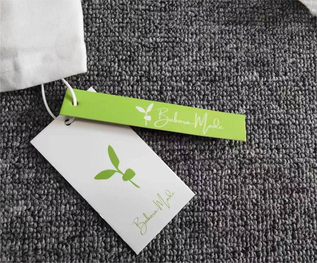Weiße Stofftasche mit grünem Etikett, Barbara Mode Logo, auf grauem Teppich.