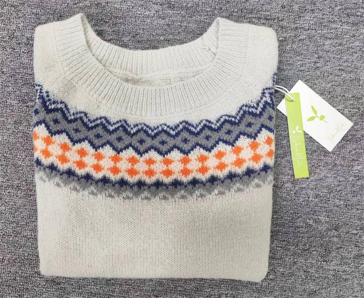 Beigefarbener Strickpullover mit blau-orangefarbenem Zickzackmuster auf grauem Hintergrund.