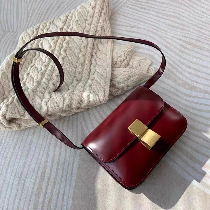Dunkelrote Ledertasche mit goldener Schnalle auf cremefarbenem Strickpullover.
