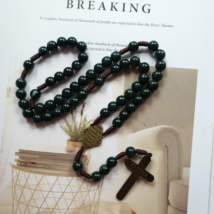 Dunkelgrüner Rosenkranz mit Kreuzanhänger, Holzperlen, religiöses Schmuckstück auf Tisch.