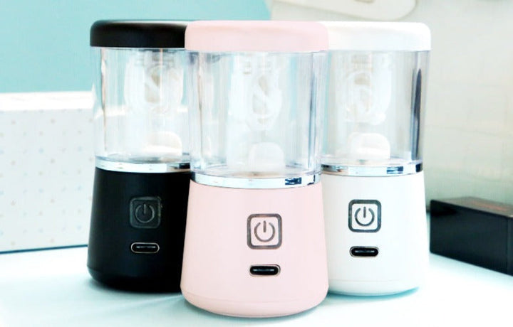 Drei tragbare Mixer in Schwarz, Rosa und Weiß, USB-aufladbar, auf blauem Hintergrund.