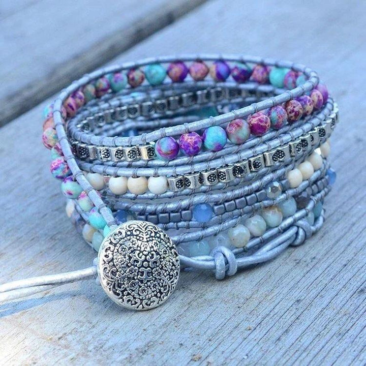 Mehrfarbiges Wickelarmband mit Edelsteinen und silbernem Verschluss auf Holzoberfläche.