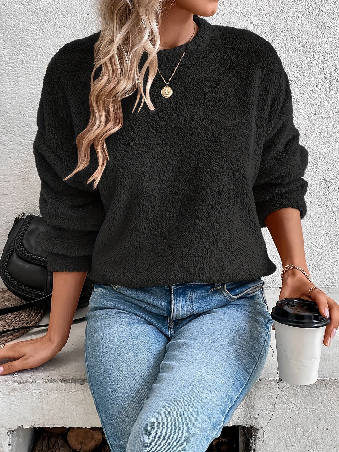 Frau in schwarzem Fleece-Pullover, blaue Jeans, hält Kaffeebecher, modisch, lässig, Herbstoutfit.