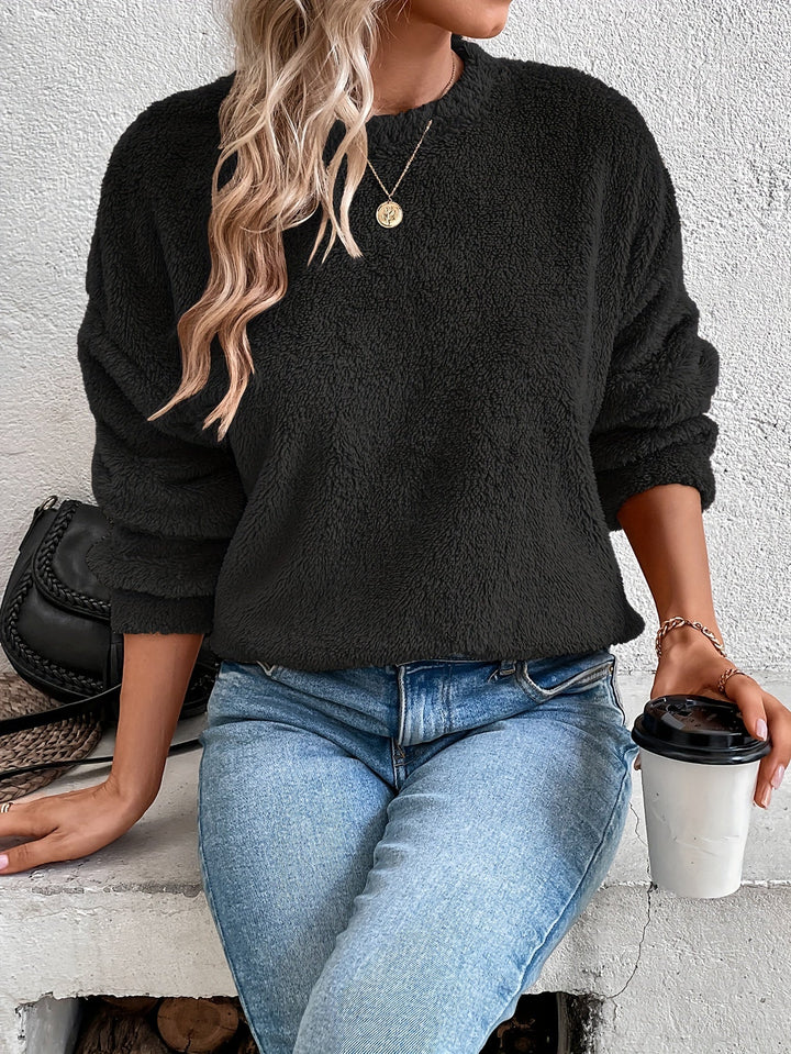 Frau in schwarzem Fleece-Pullover, blaue Jeans, hält Kaffeebecher, modisch, lässig, Herbstoutfit.