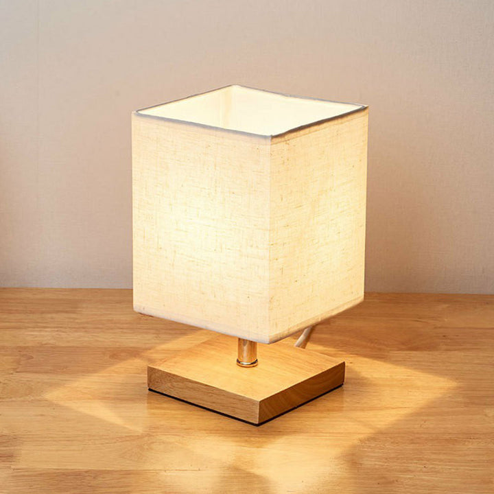 Beige Tischlampe mit quadratischem Stoffschirm auf Holzsockel, moderne Wohnraumbeleuchtung.