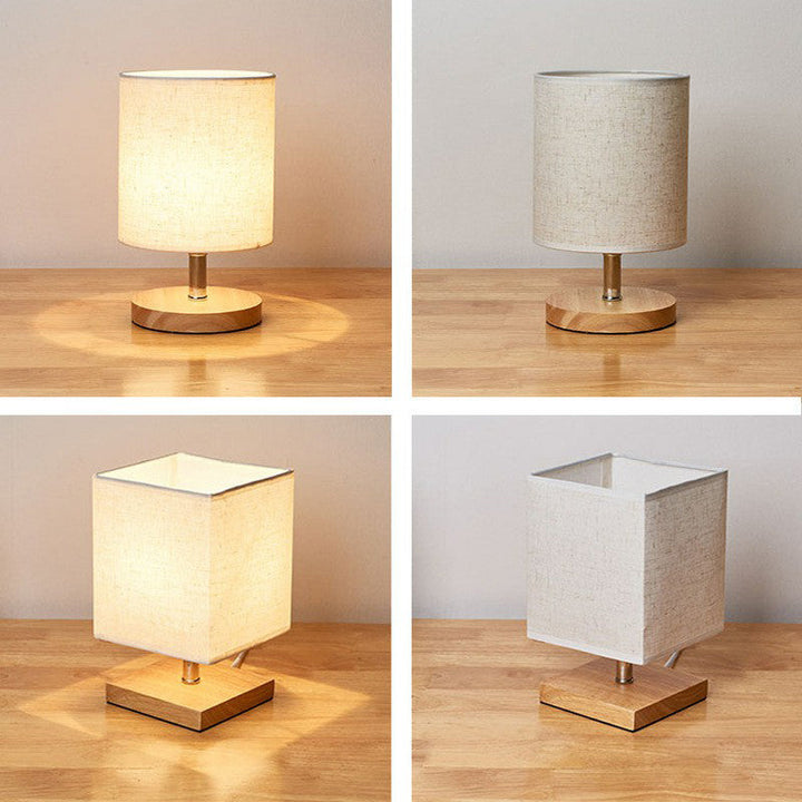 Vier Tischlampen mit Holzsockel und Stoffschirm, rund und quadratisch, auf Holztisch.
