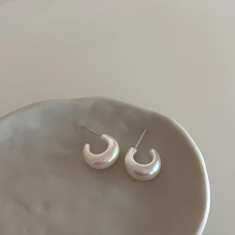 Crescentförmige Perlenohrringe auf Keramikschale, minimalistisch, elegant, Schmuckdesign.
