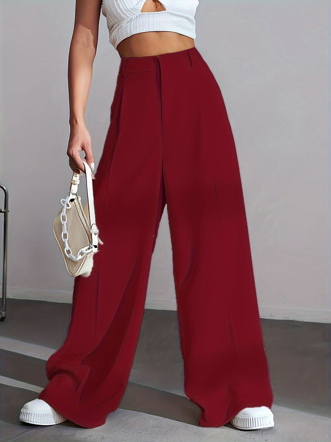 Frau in weinroter Hose, weißem Top, hält weiße Handtasche, modisch, elegant, Streetwear.