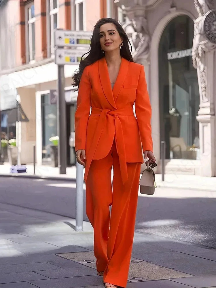 Frau in orangefarbenem Blazer mit Gürtel und passender Hose auf städtischer Straße.
