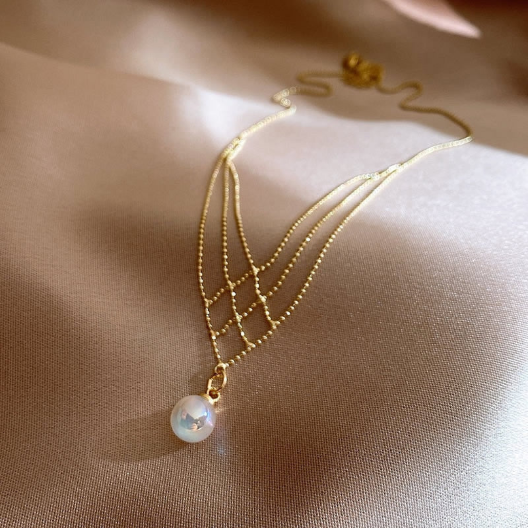 Goldene Halskette mit Perlenanhänger auf beigem Hintergrund, eleganter Schmuck für Damen.