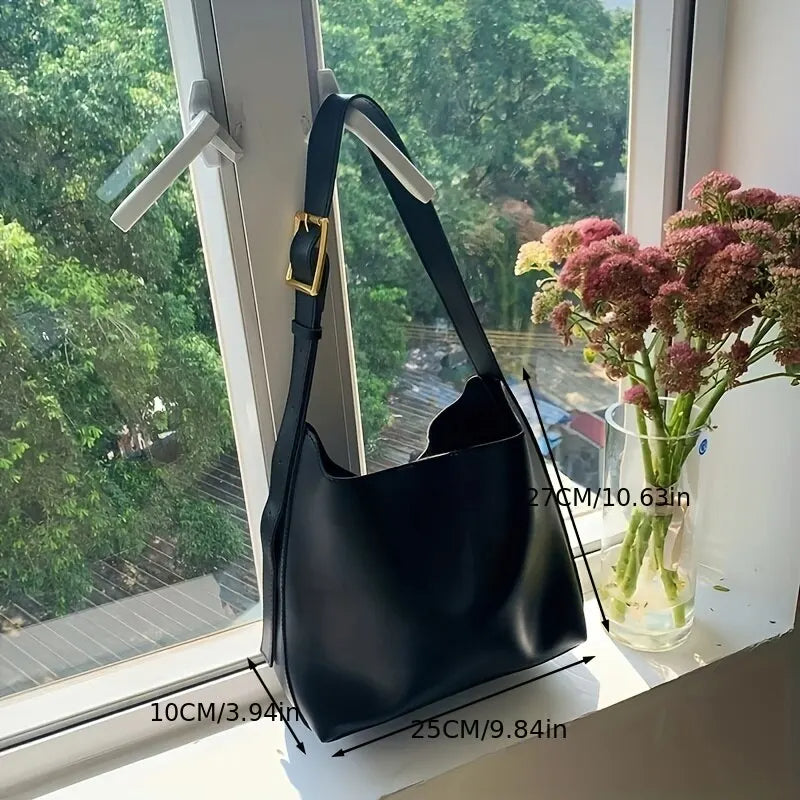 Schwarze Ledertasche mit verstellbarem Riemen, goldener Schnalle, auf Fensterbank.