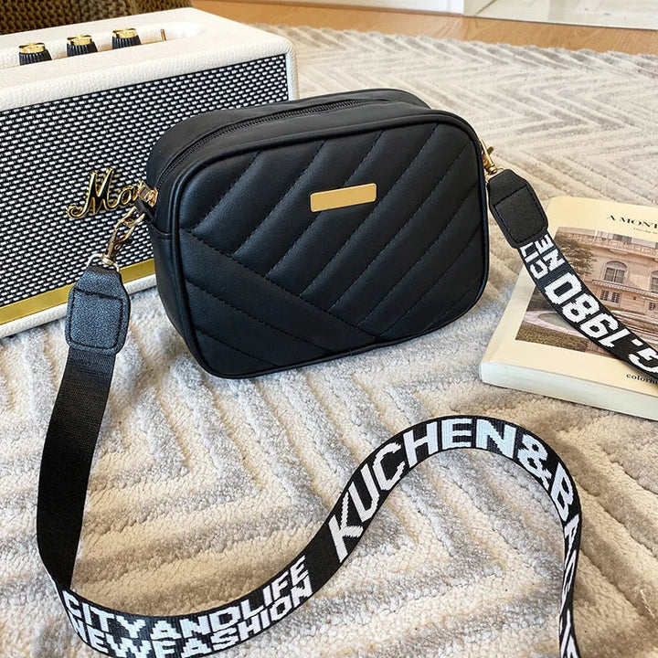 Schwarze Umhängetasche aus Leder mit gestepptem Design auf Teppich, modisch und elegant.