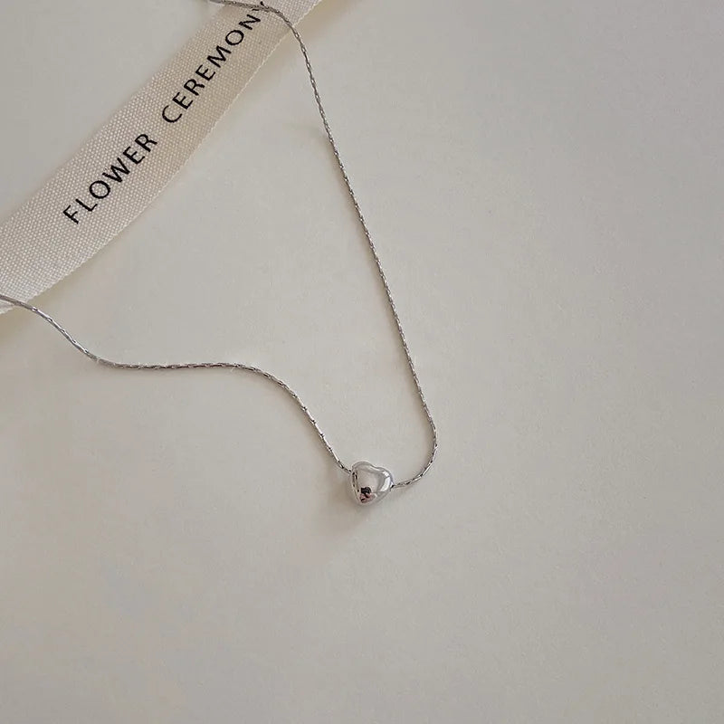 Silberne Herz-Halskette auf beigem Hintergrund, minimalistisch, elegantes Schmuckdesign.