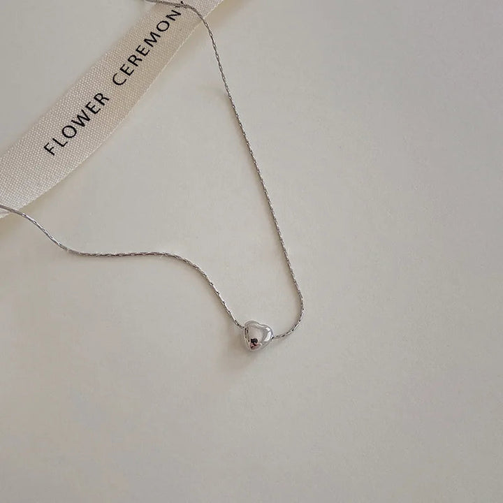 Silberne Herz-Halskette auf beigem Hintergrund, minimalistisch, elegantes Schmuckdesign.