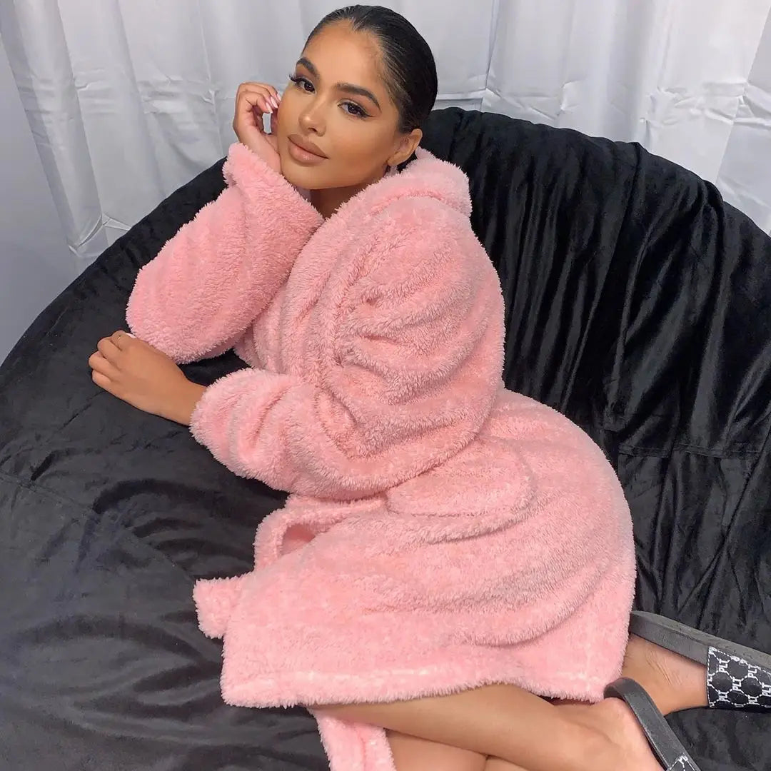 Frau in rosa Fleece-Bademantel auf schwarzem Sitzsack, gemütliche Mode, Innenraum.