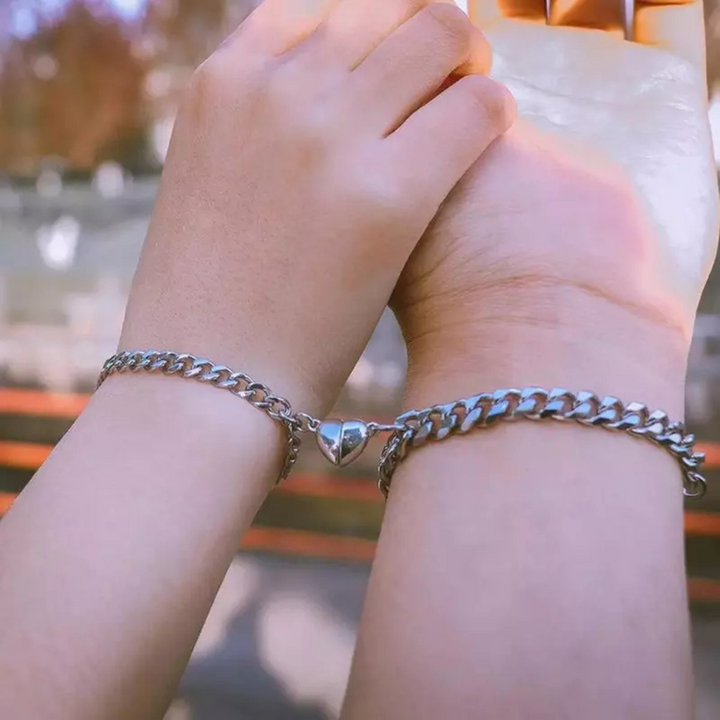Zwei Hände mit silbernen Partnerarmbändern, Herzanhänger, Edelstahl, Freundschaftsschmuck.