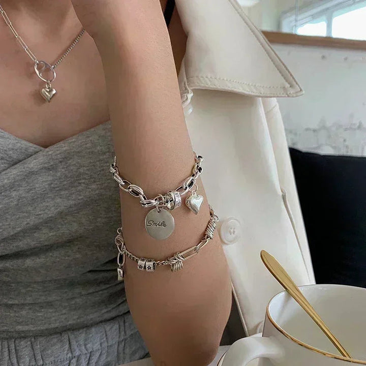 Frau mit silbernem Armband und Herzanhänger, graues Kleid, weiße Jacke, Kaffeetasse.