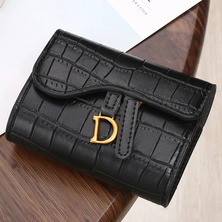 Schwarze Leder-Geldbörse mit Krokodilprägung und goldener Schnalle auf Holztisch.
