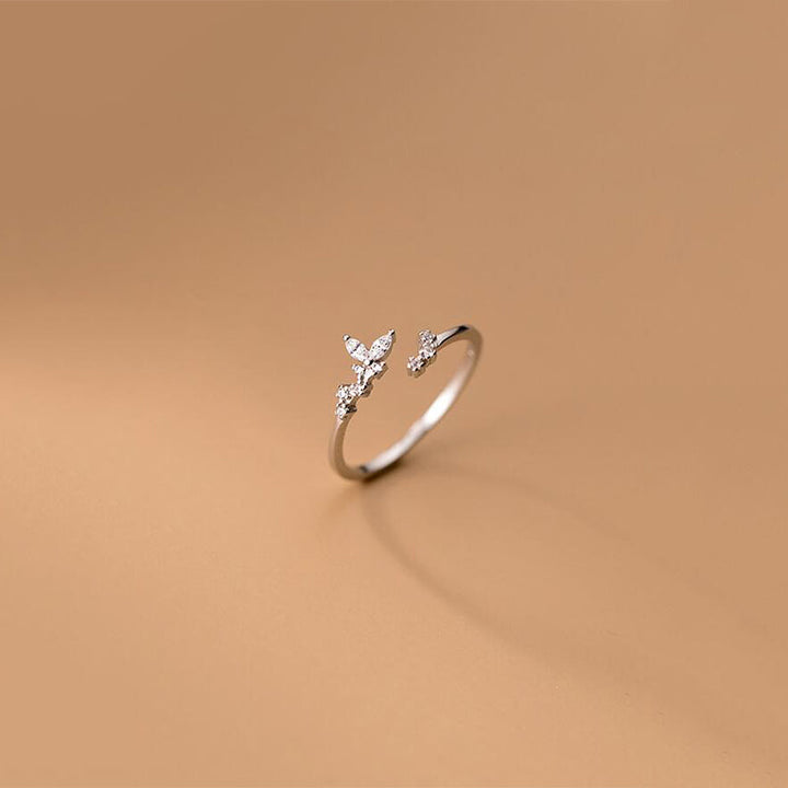 Silberner offener Ring mit Schmetterlingsdesign und Zirkonia-Steinen auf beigem Hintergrund.