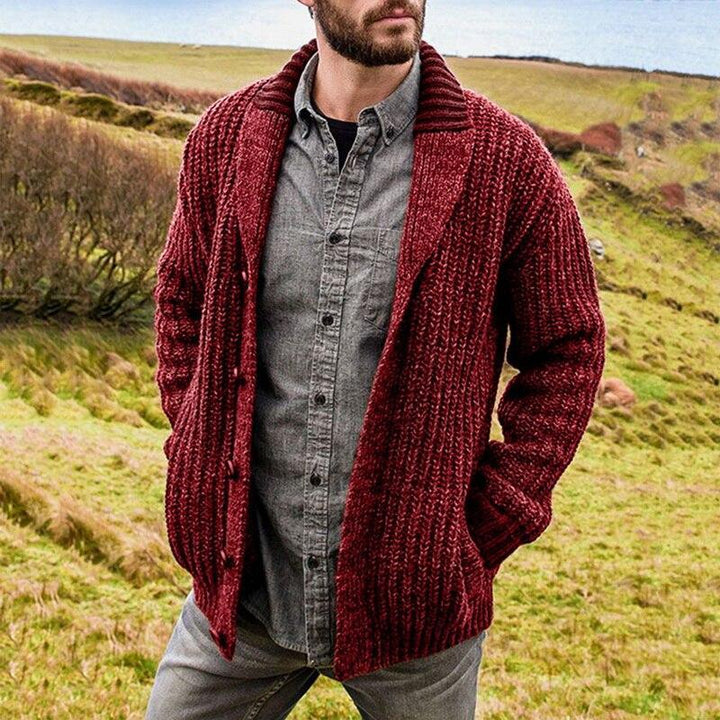 Mann in roter Strickjacke und grauem Hemd in ländlicher Landschaft.