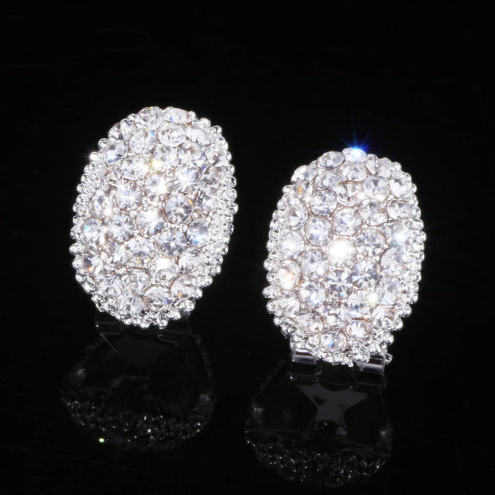 Ovale silberne Ohrringe mit Kristallsteinen, funkelnd, eleganter Schmuck, schwarzer Hintergrund.