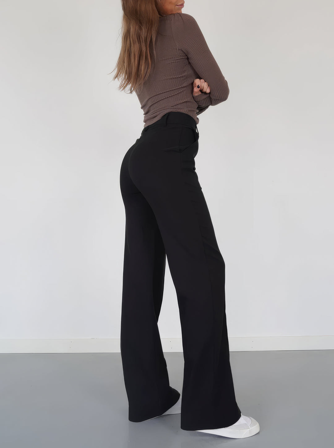Frau in schwarzer Schlaghose und braunem Oberteil, seitlich, weiße Sneaker, minimalistischer Stil.