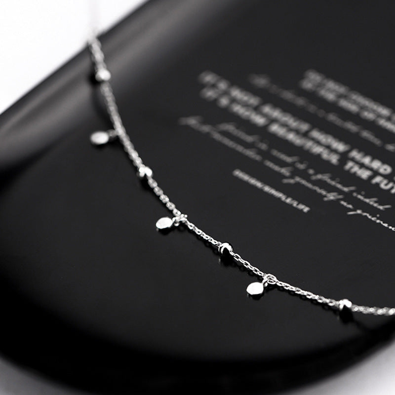 Silberne Halskette mit kleinen Anhängern auf schwarzem Hintergrund, eleganter Schmuck.