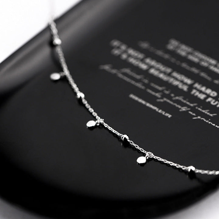 Silberne Halskette mit kleinen Anhängern auf schwarzem Hintergrund, eleganter Schmuck.