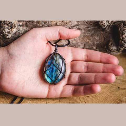 Hand hält blauen Labradorit-Anhänger, handgefertigt, in Drahtfassung, Schmuck, Naturstein.