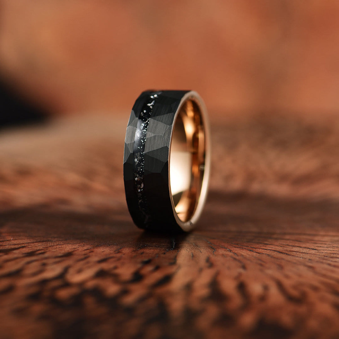 Schwarzer Wolframring mit facettierter Oberfläche und goldener Innenseite auf Holzoberfläche.