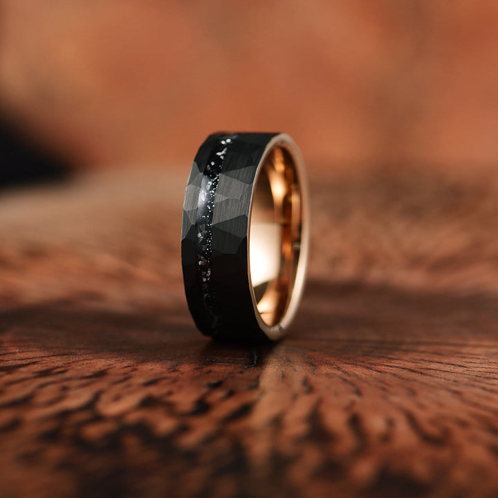 Schwarzer Wolframring mit facettierter Oberfläche und goldener Innenseite auf Holzoberfläche.