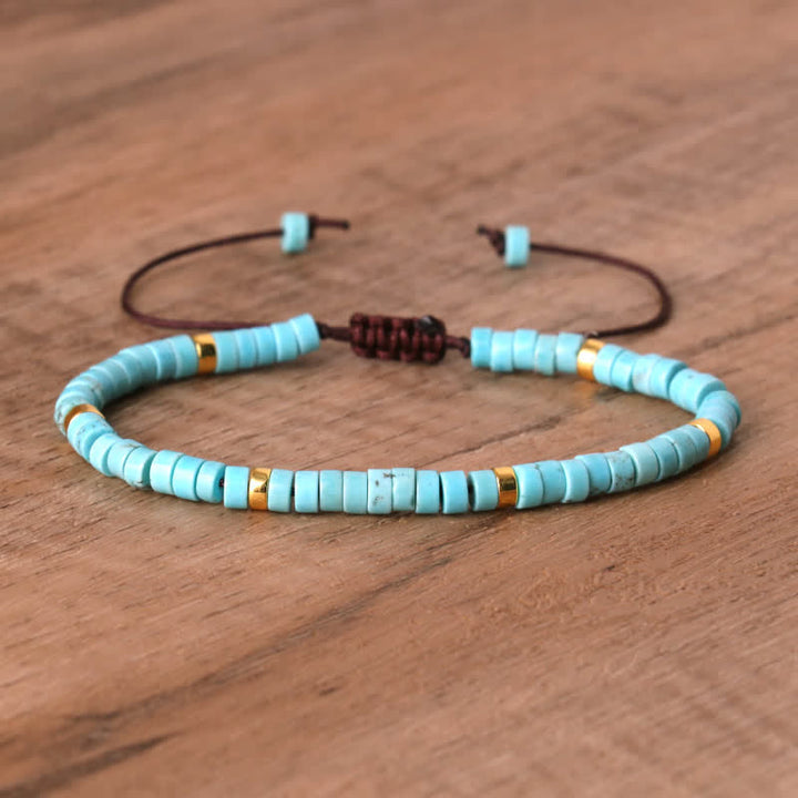 Armband aus türkisfarbenen Perlen mit goldenen Akzenten, verstellbares braunes Band, Holzoberfläche.