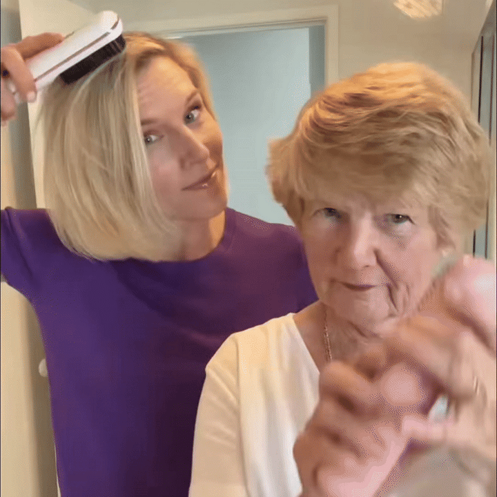 Blonďatá žena v fialovém triku si přikládá bílý kartáč k vlasům, před ní stojí starší dáma s krátkým účesem. 9
