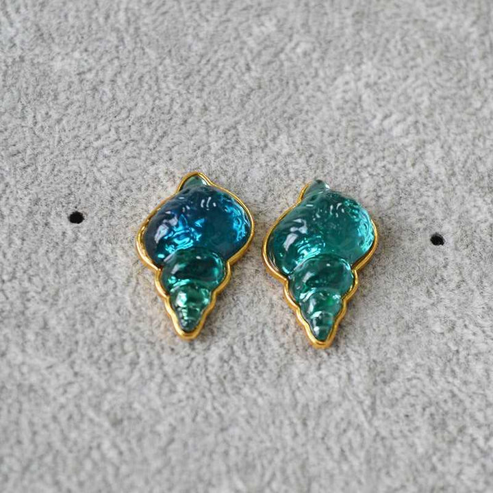 Blaue und grüne Muschel-Ohrringe, goldumrandet, auf grauem Hintergrund, Modeschmuck.