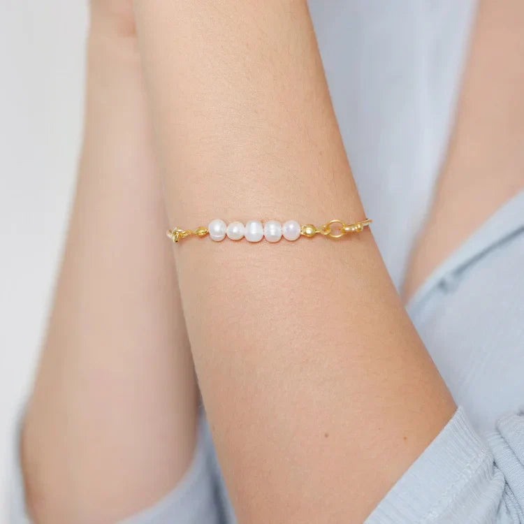 Goldenes Armband mit weißen Perlen, eleganter Schmuck, Damenaccessoire, Nahaufnahme.