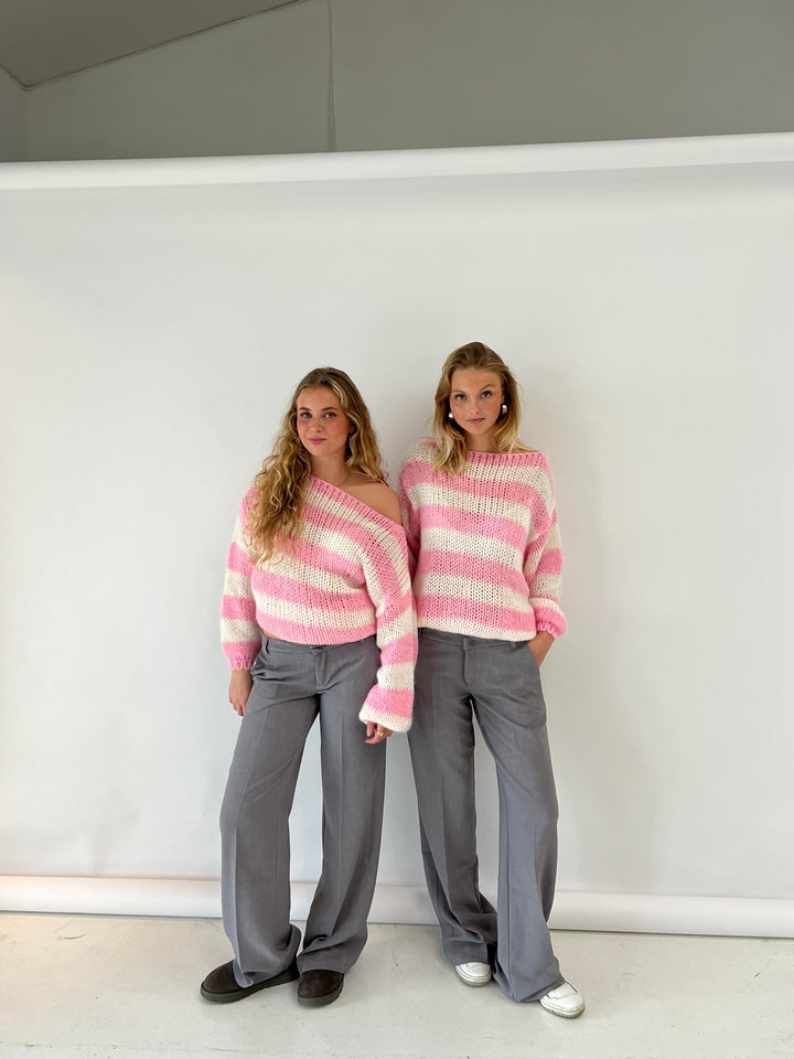 Zwei Frauen in gestreiften rosa Pullovern und grauen Hosen vor weißem Hintergrund.
