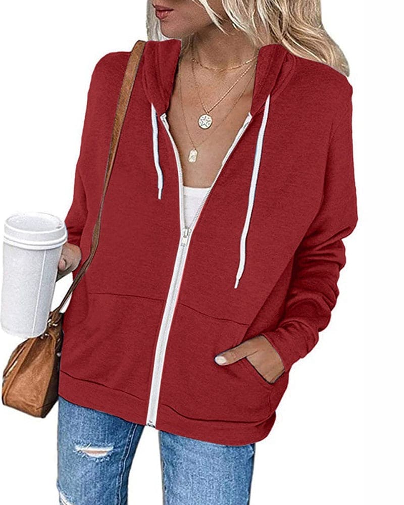 Frau in rotem Kapuzenpullover, Jeans, mit Kaffeebecher und brauner Tasche.