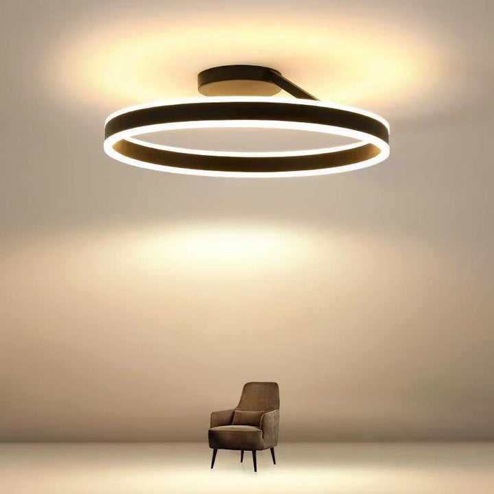 Moderne LED-Deckenleuchte, schwarz, rund, energiesparend, über braunem Sessel im Wohnzimmer.