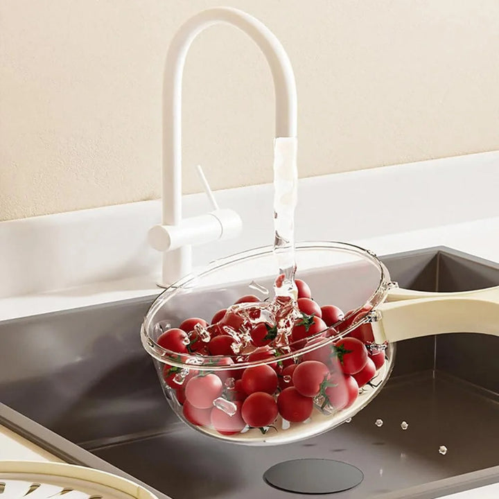 Durchsichtiger Kunststoffsieb mit roten Kirschtomaten unter Wasserhahn in moderner Küche.