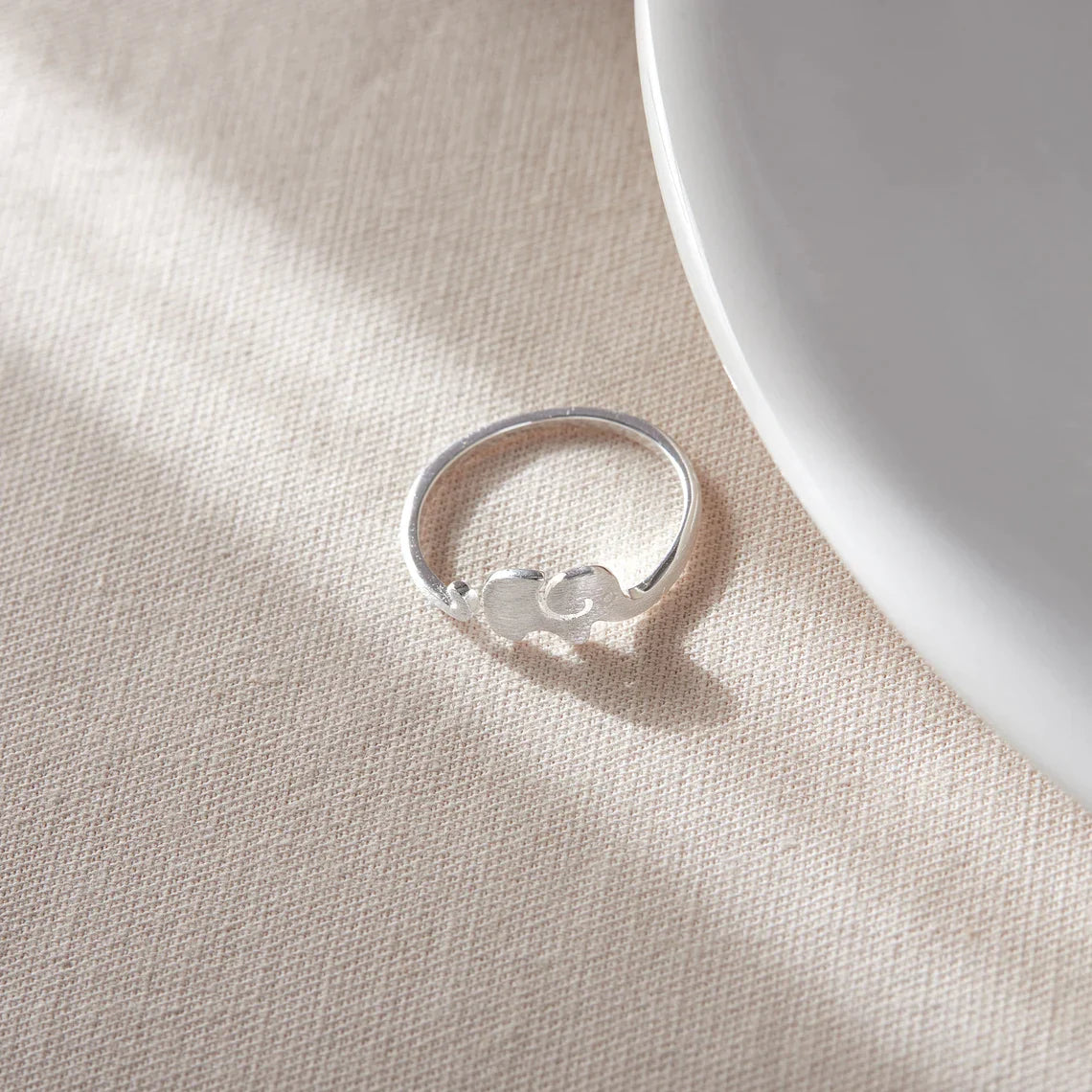 Silberner Verlobungsring mit Herzdesign auf beigem Stoff, eleganter Schmuck für Damen.