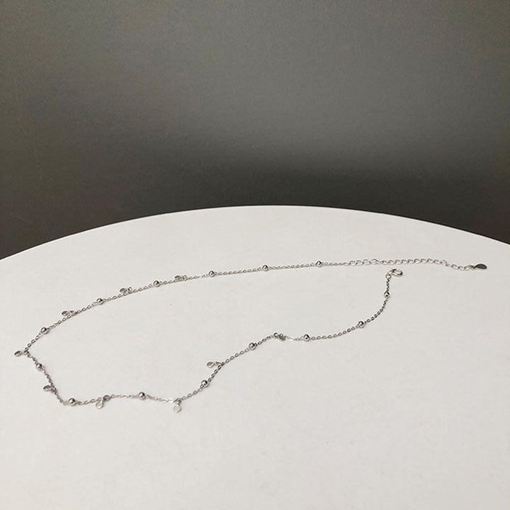 Silberne Halskette mit kleinen Anhängern auf weißem Tisch, minimalistisches Schmuckdesign.