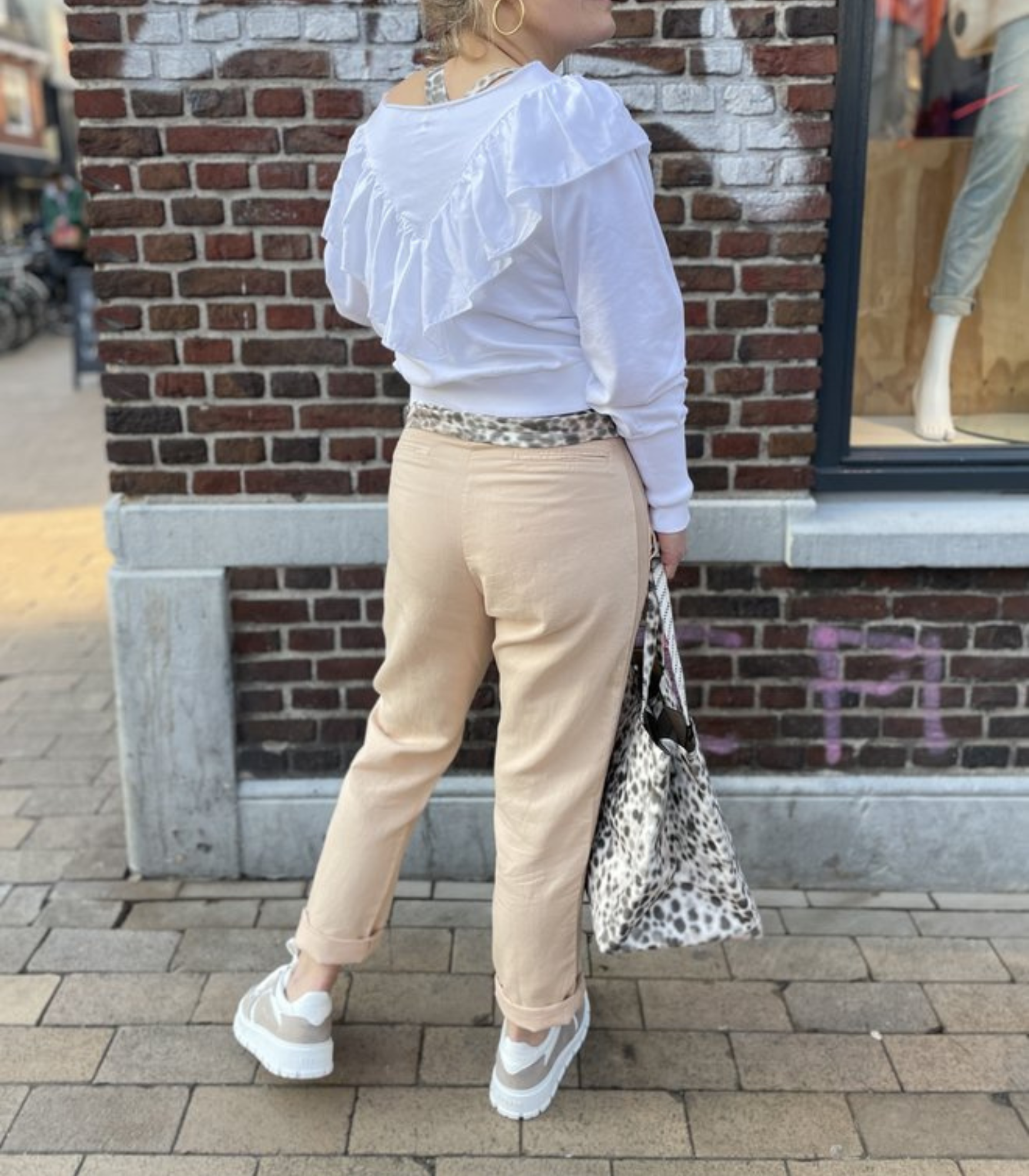 Frau in weißem Rüschenpullover und beigen Jeans mit Leopardenmuster-Tasche auf Straße.