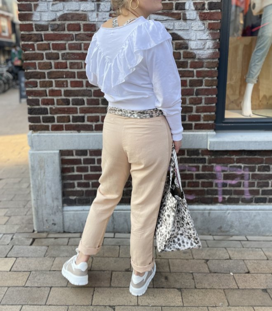 Frau in weißem Rüschenpullover und beigen Jeans mit Leopardenmuster-Tasche auf Straße.