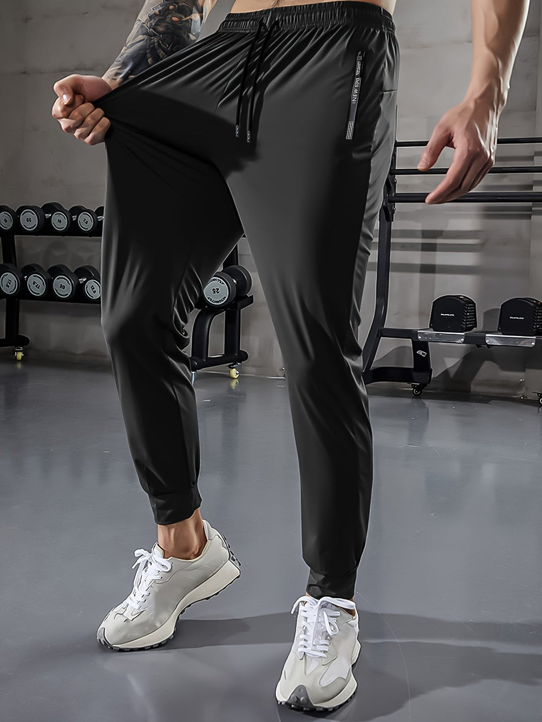 Mann in schwarzer Sporthose im Fitnessstudio, Hanteln im Hintergrund, weiße Turnschuhe.